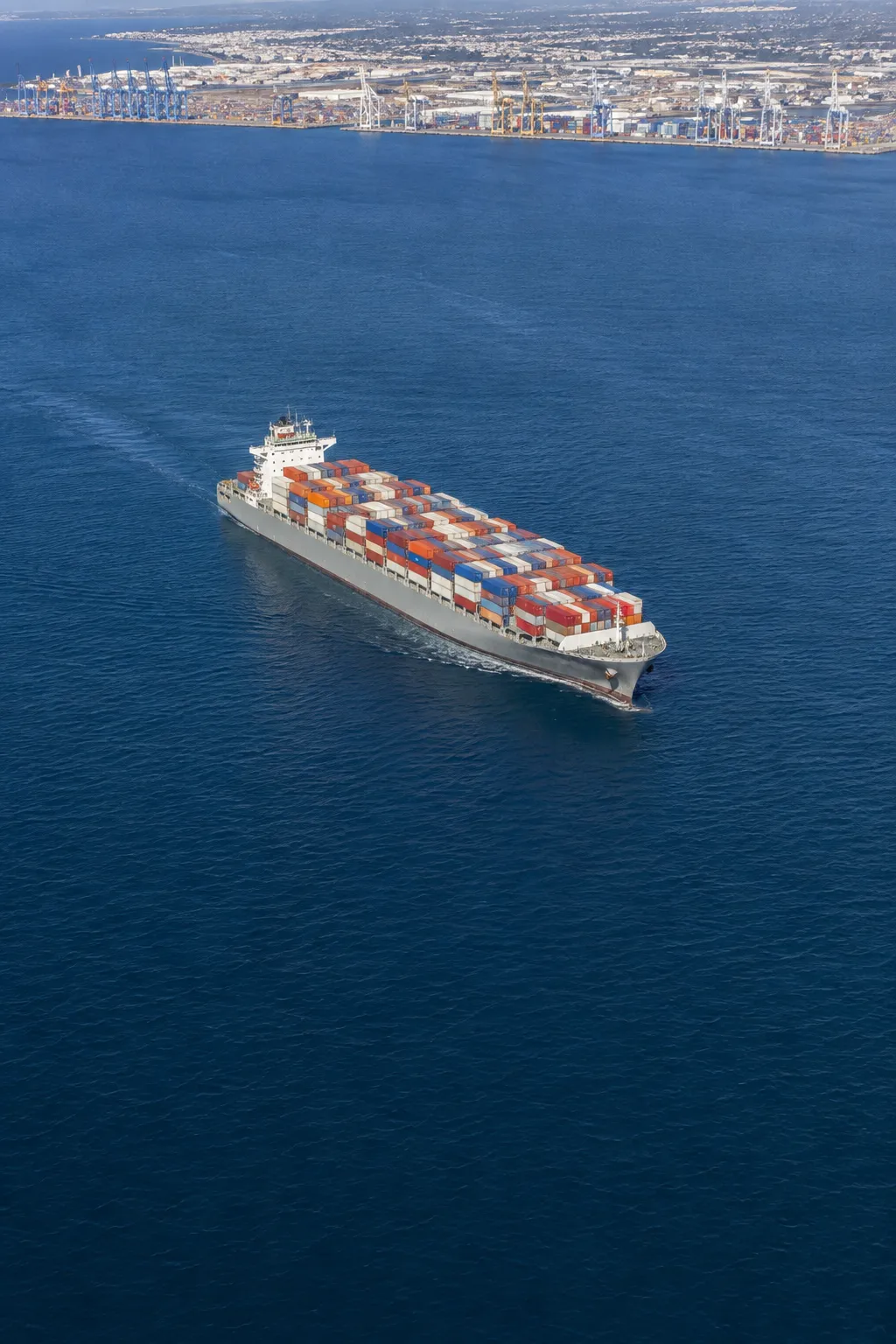 Illustrative aerial view of a container ship beside a coastal terminal